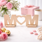 Wooden decorative letters spelling 'MOM' with flowers and a gift in the background
